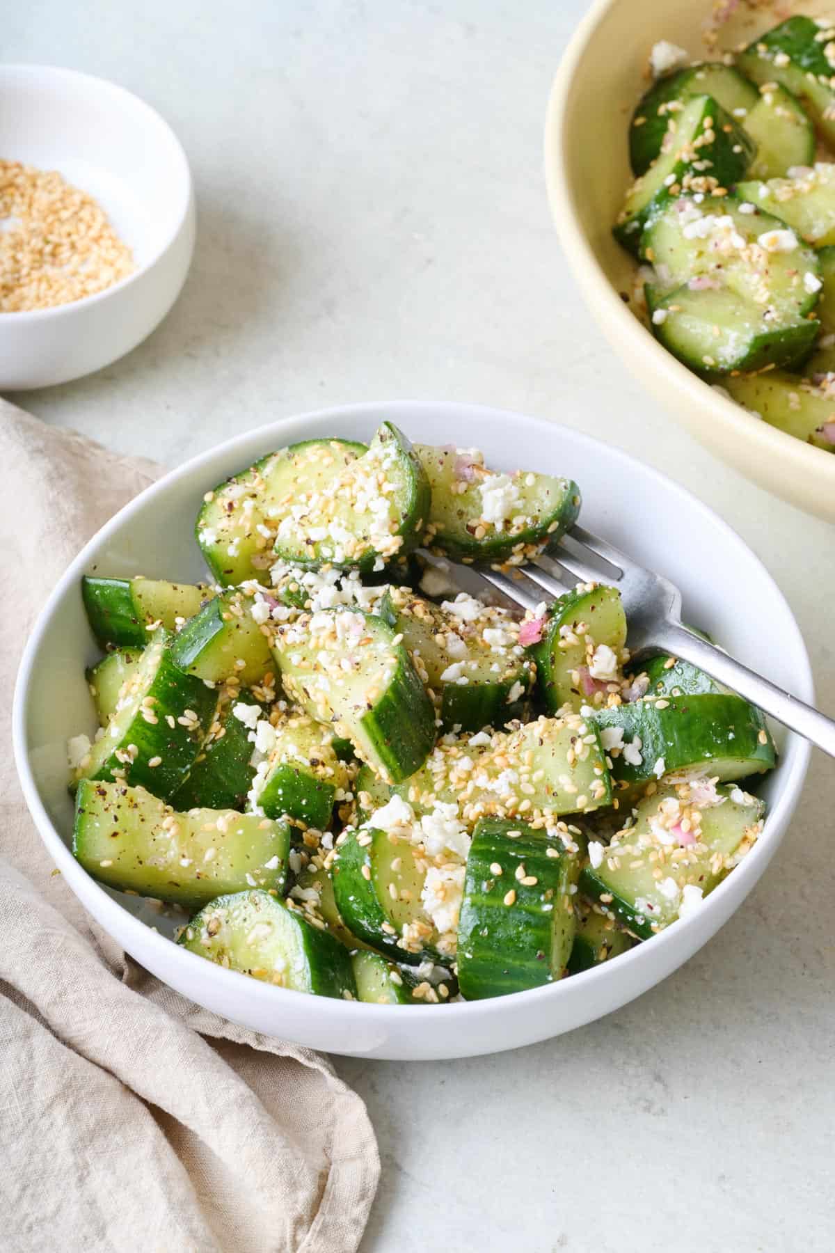 Smashed cucumber salad in a bowl with feta and sesame seeds.