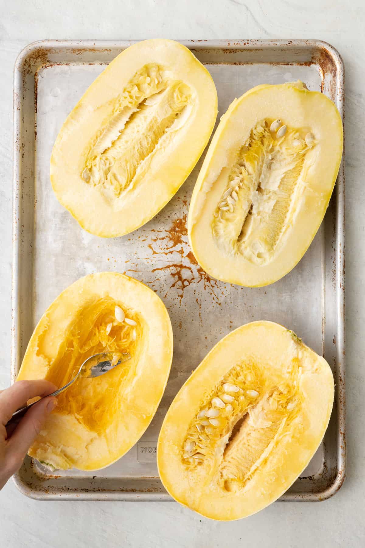 Halved spaghetti squashes with seeds being scooped out.