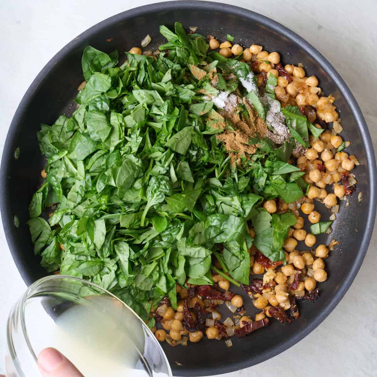 Spinach and seasonings added to skillet with lemon juice being poured in.