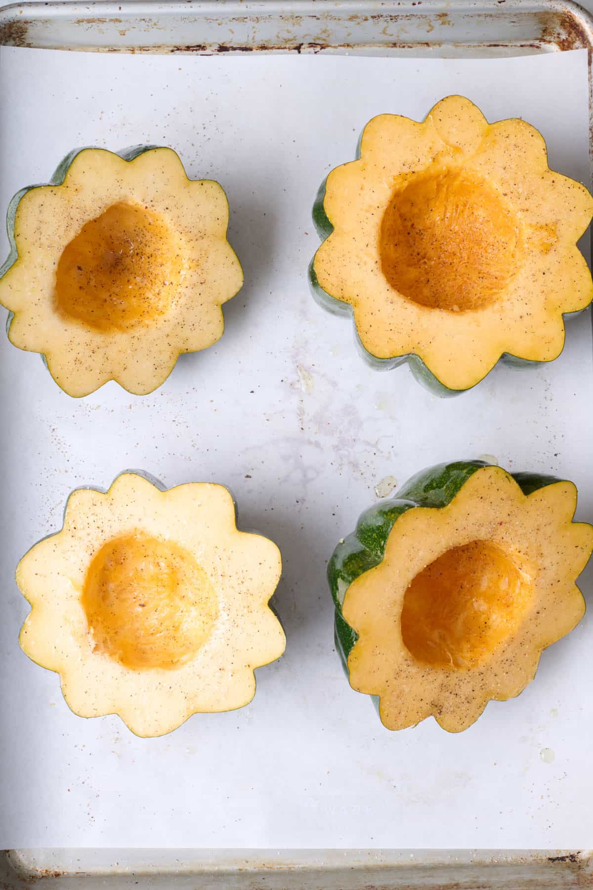 Acorn squash halves seasoned with oil, salt and pepper on a parchment lined baking sheet, cut side up.