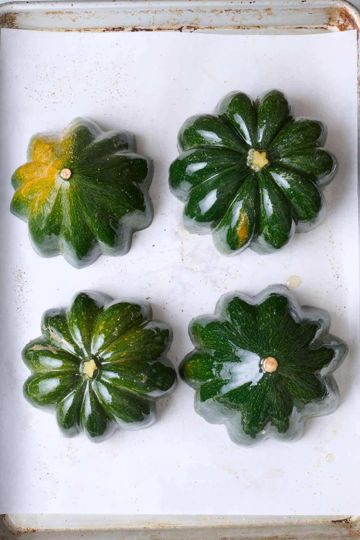 Four acorn squash halves cut side down on baking sheet.