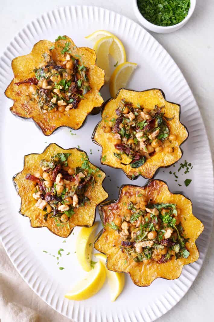 Vegetarian stuffed acorn squash on a large platter, garnished with lemon wedges and fresh parsley.