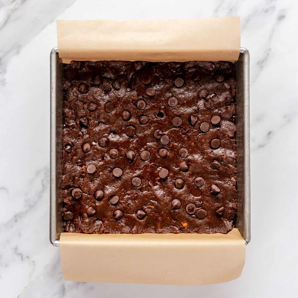 Batter added to a square baking pan lined with parchment paper with extra chocolate chips on top.