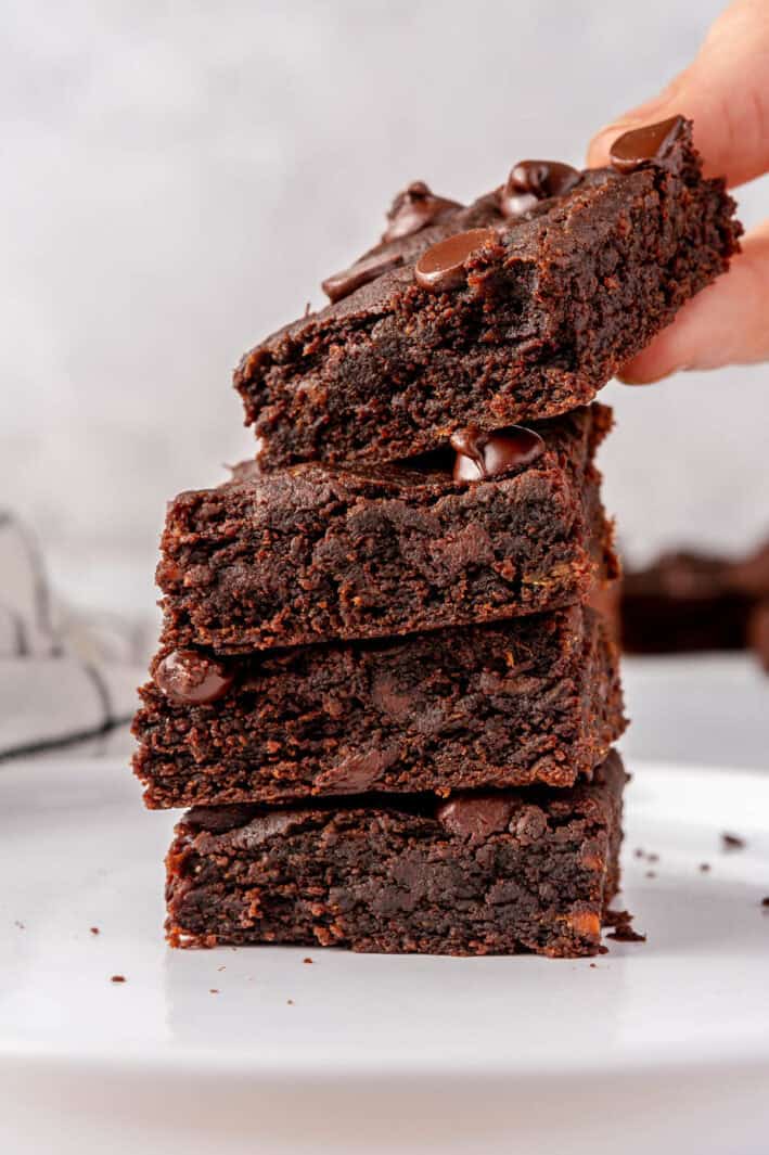 Fudgy sweet potato brownies stacked up with a hand lifting one up.