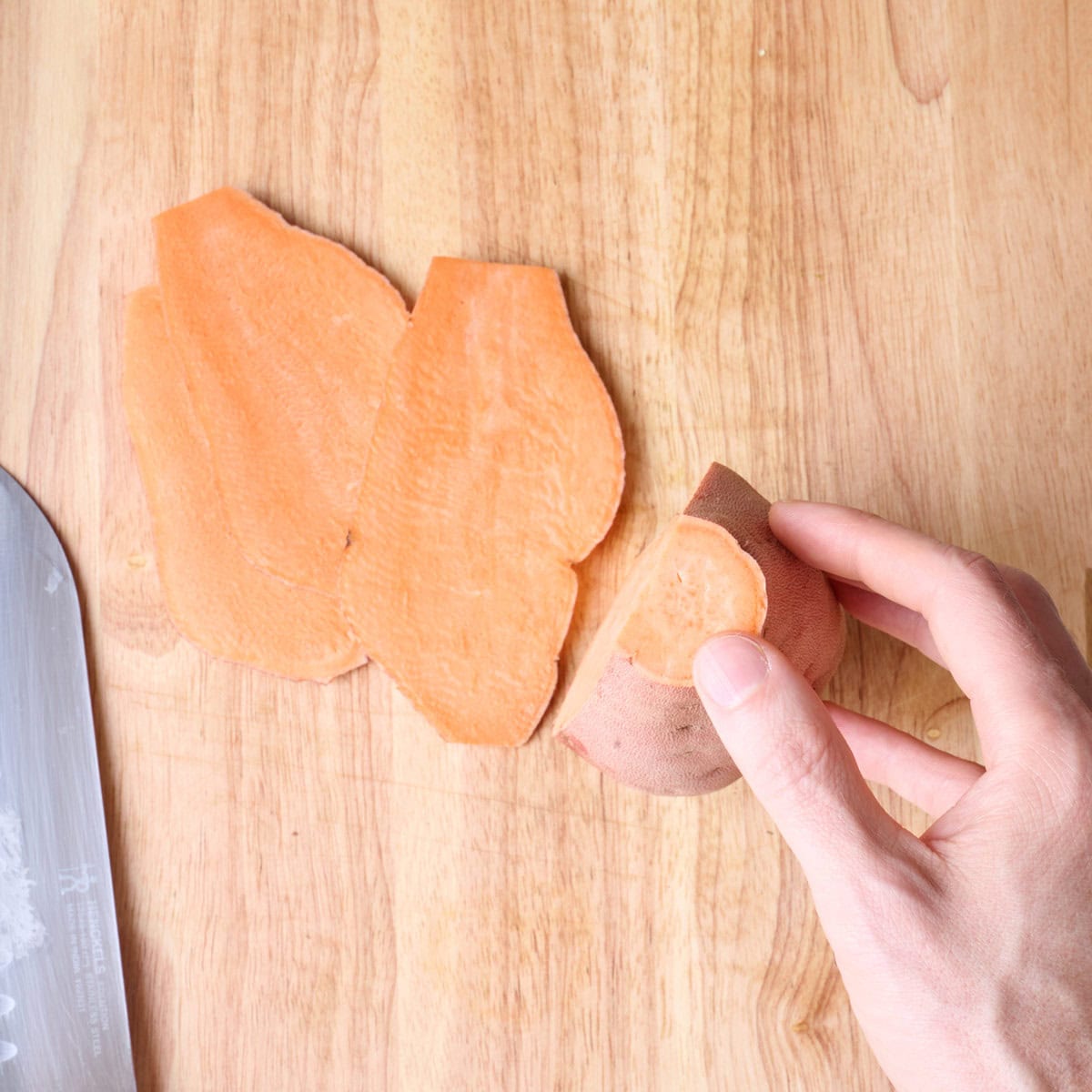 Sweet potato on a cutting board being sliced into planks.