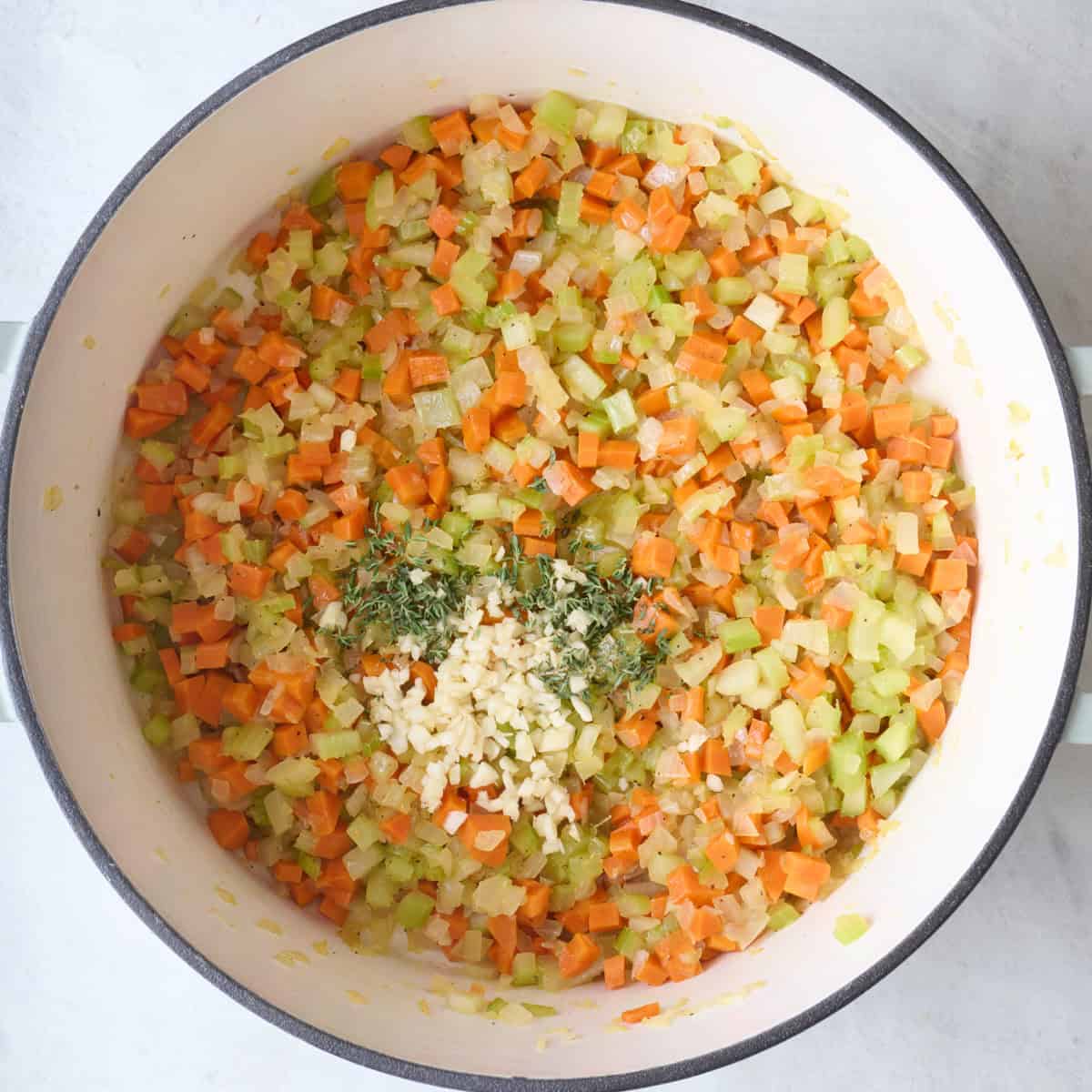 Garlic and chopped herbs added to cooked veggies in a pot.