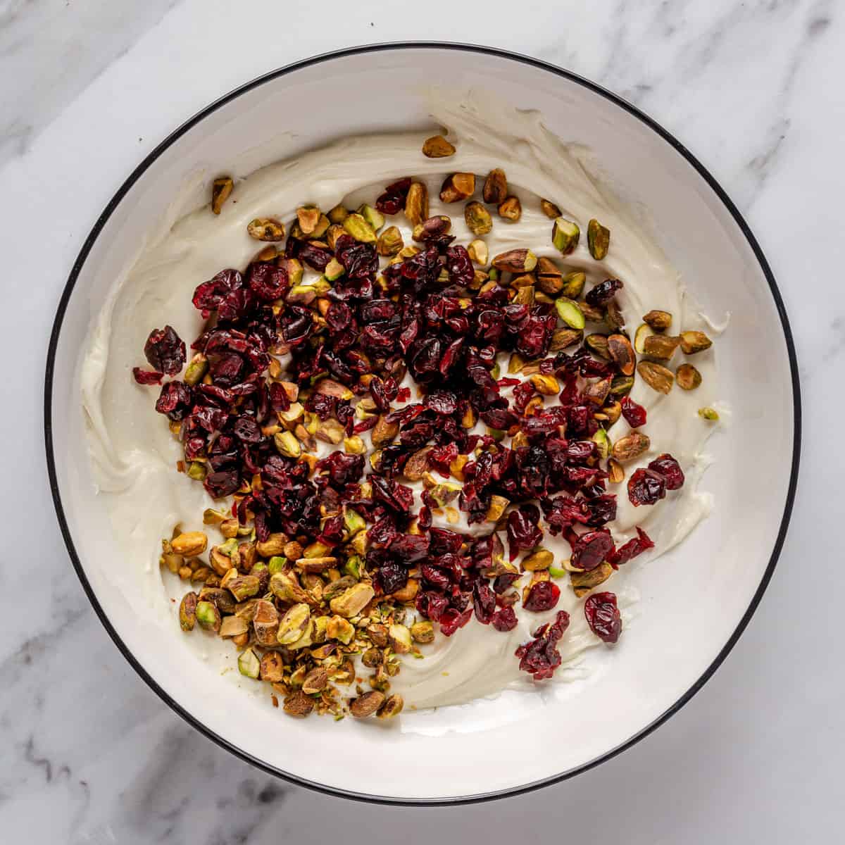 Melted white chocolate in a bowl with dried cranberries and pistachios added on top.