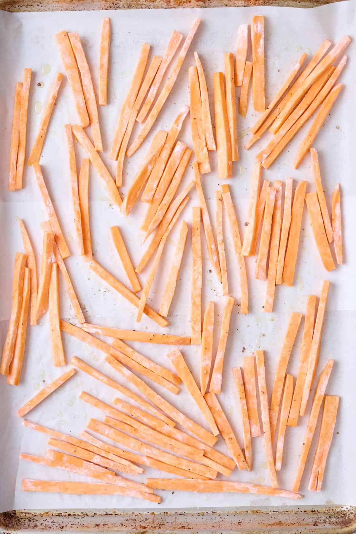 Coated potato sticks on a parchment lined baking sheet.