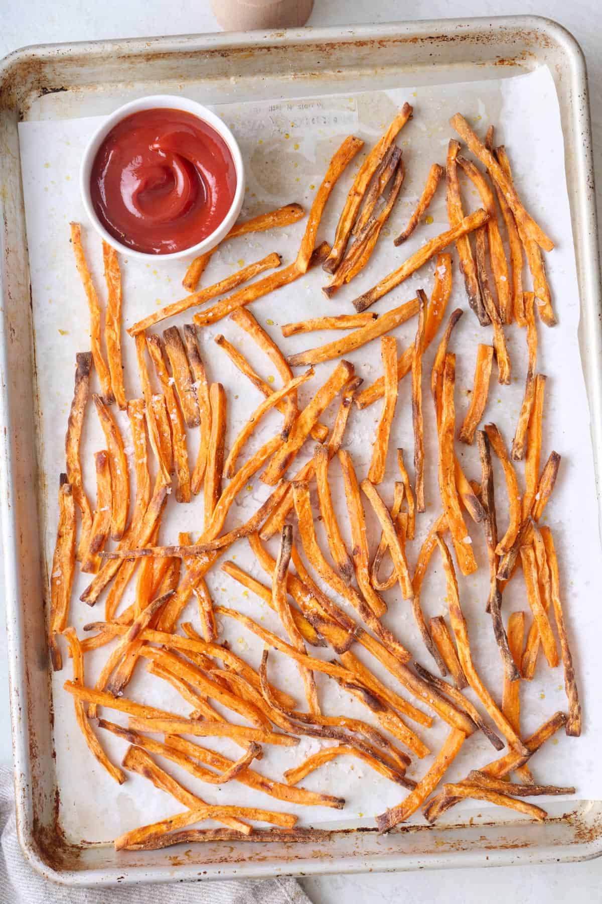 Sweet potato fries on a sheet pan with a small dish of ketchp.