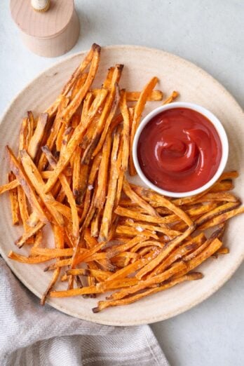 Baked sweet potato fries on a plate with a small dish of ketchup for dipping.