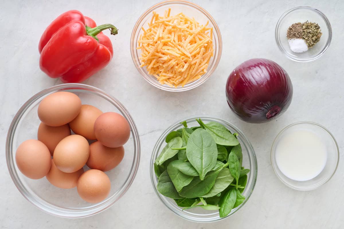 Ingredient for recipe before prepping: red pepper, eggs, shredded cheese, spinach, red onion, milk, and seasonings.