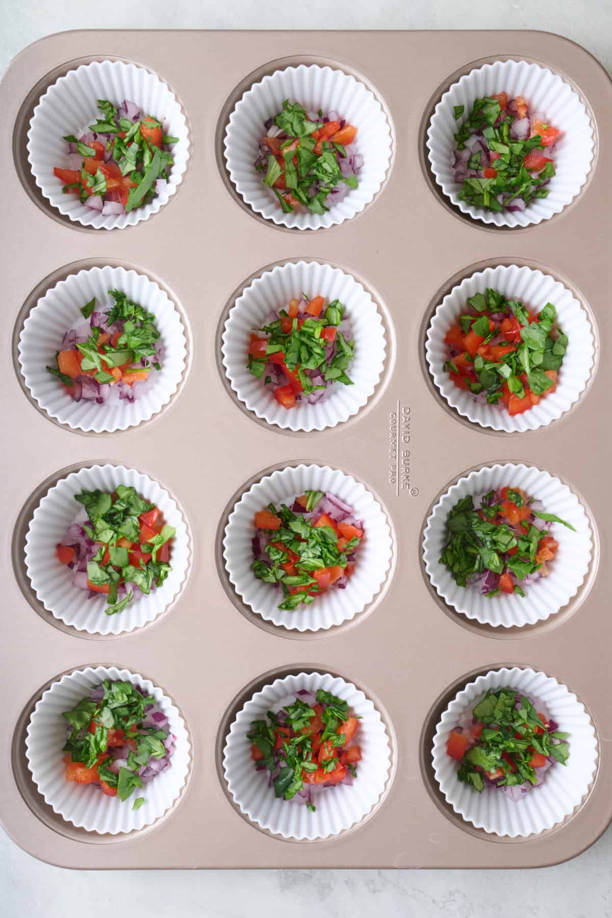 Muffin pan with silicone liners filled with chopped veggies.