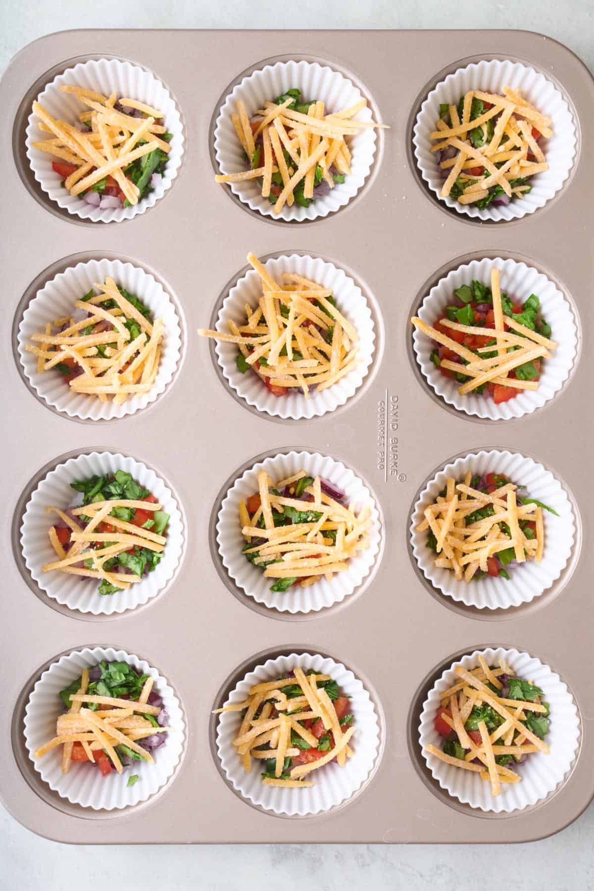 Shredded cheese added to each veggie filled muffin cup.