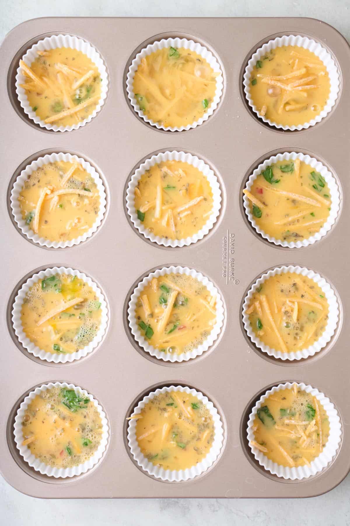 Egg mixture added to veggies in a muffin tin before baking.