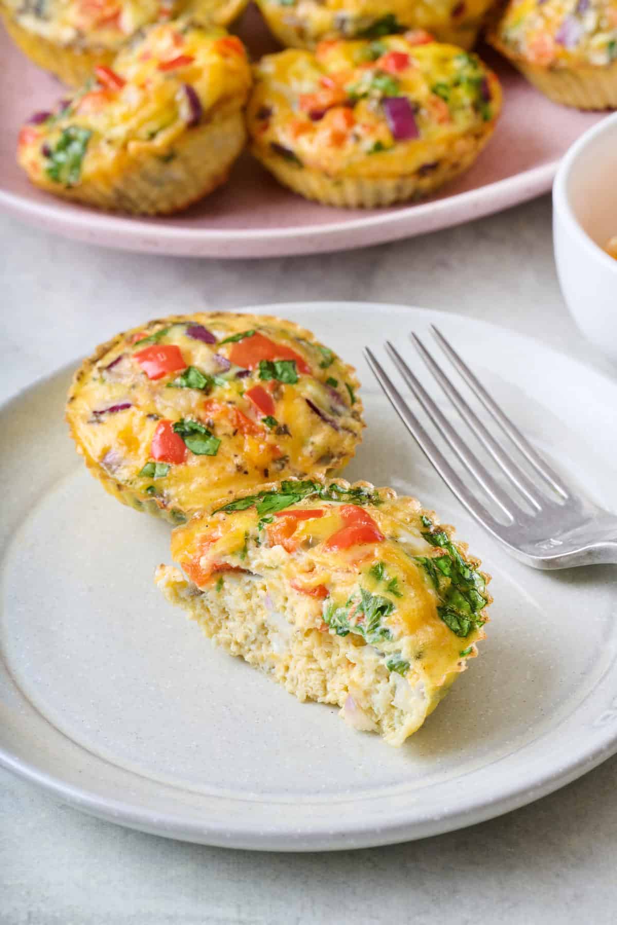 Two breakfast egg muffin cups on a plate with a bite taken out of one to show inside texture.