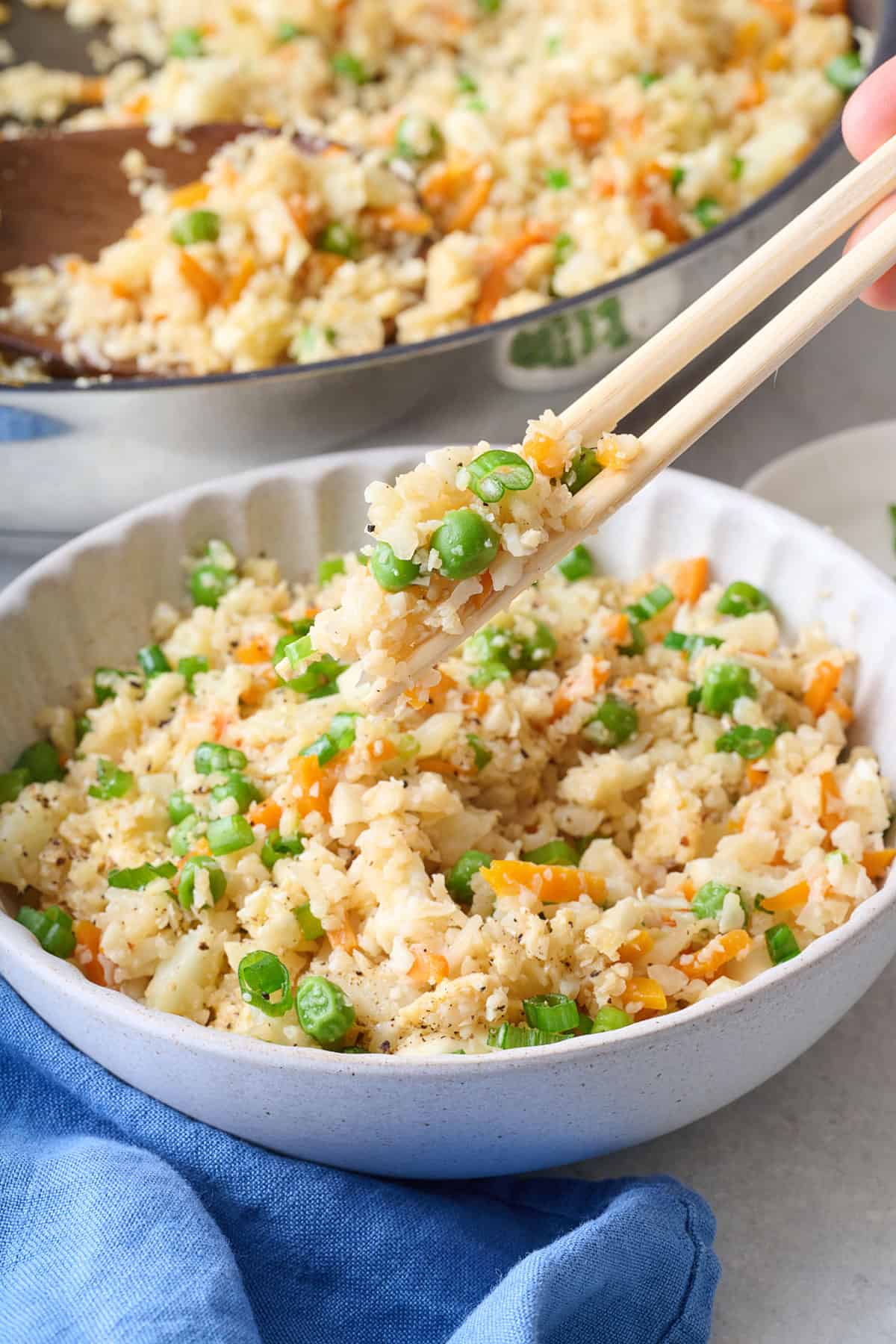 Chopsticks lifting up a bite of cauliflower rice stir fry with skillet nearby.