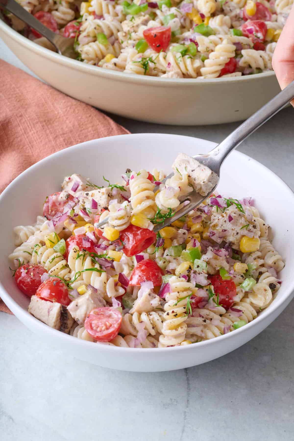 Fork lifting up a bite of pasta salad with chicken from a bowl.