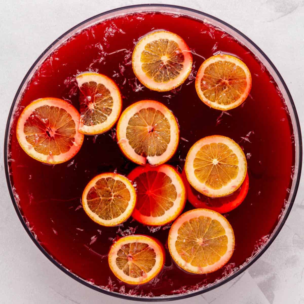 Juices, simple syrup, and orange slices added to a punch bowl.