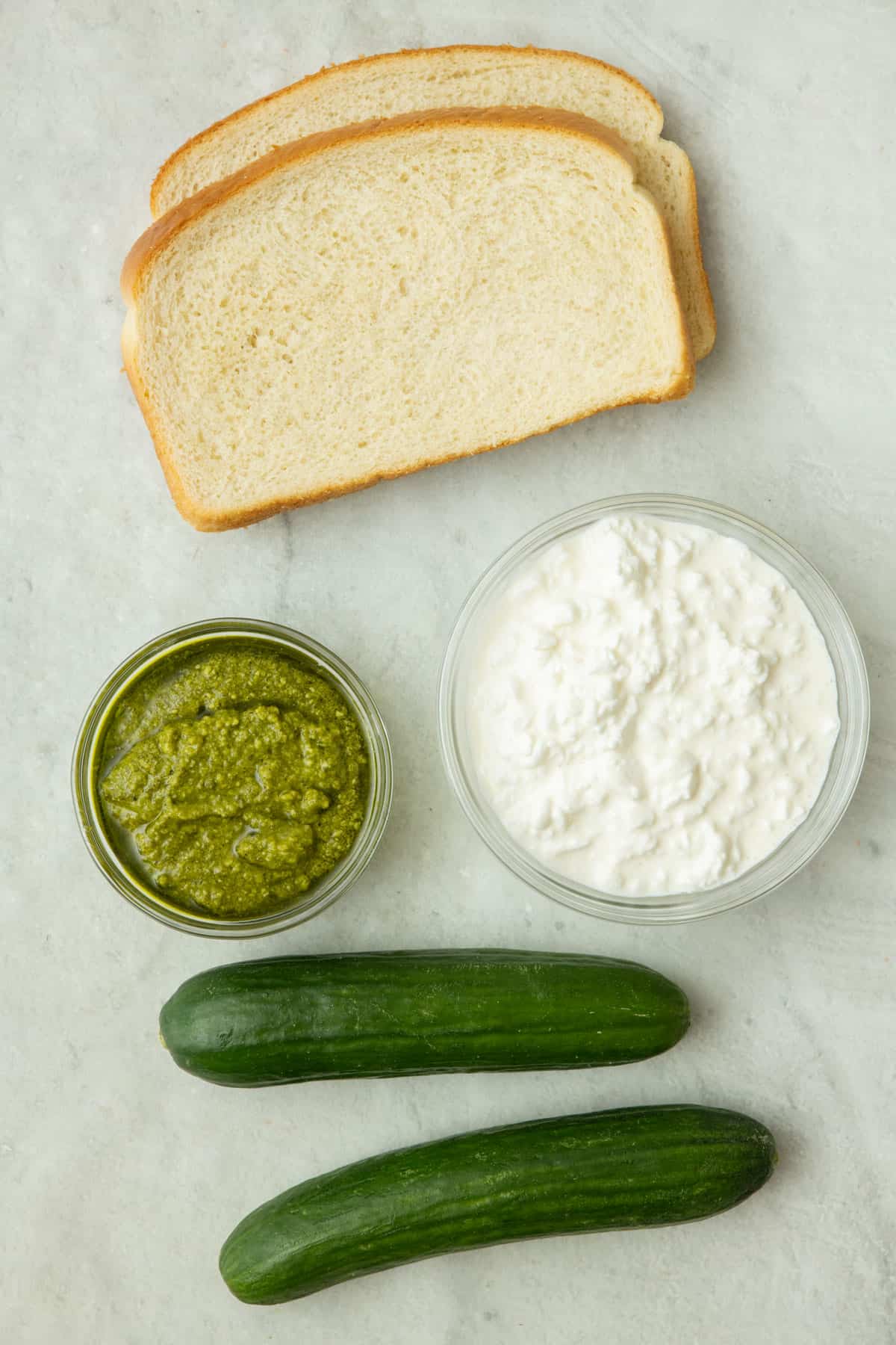 Ingredients for recipe: bread slices, cottage cheese, pesto, and cucumbers.