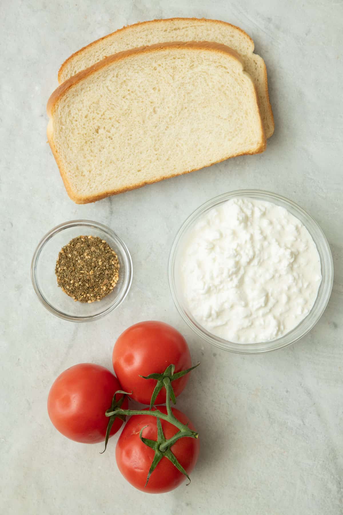 Ingredients for recipe: bread slices, cottage cheese, zaatar, and tomatoes.