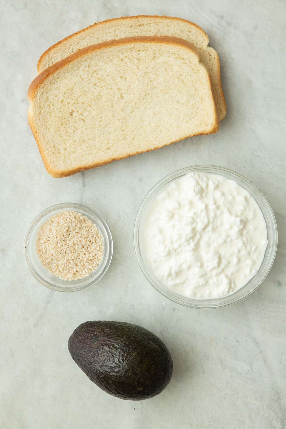 Ingredients for recipe: bread slices, cottage cheese, sesame seeds, and avocado.