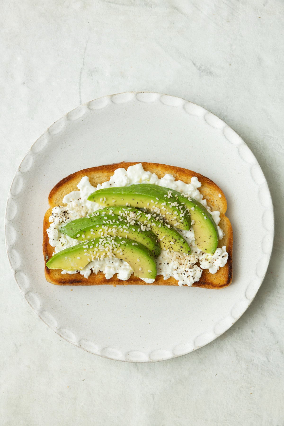 Toast with cottage cheese, avocado slices, and sesame seeds.