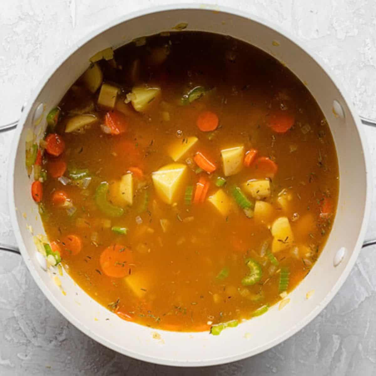 Broth added to cooked vegetables in pot.