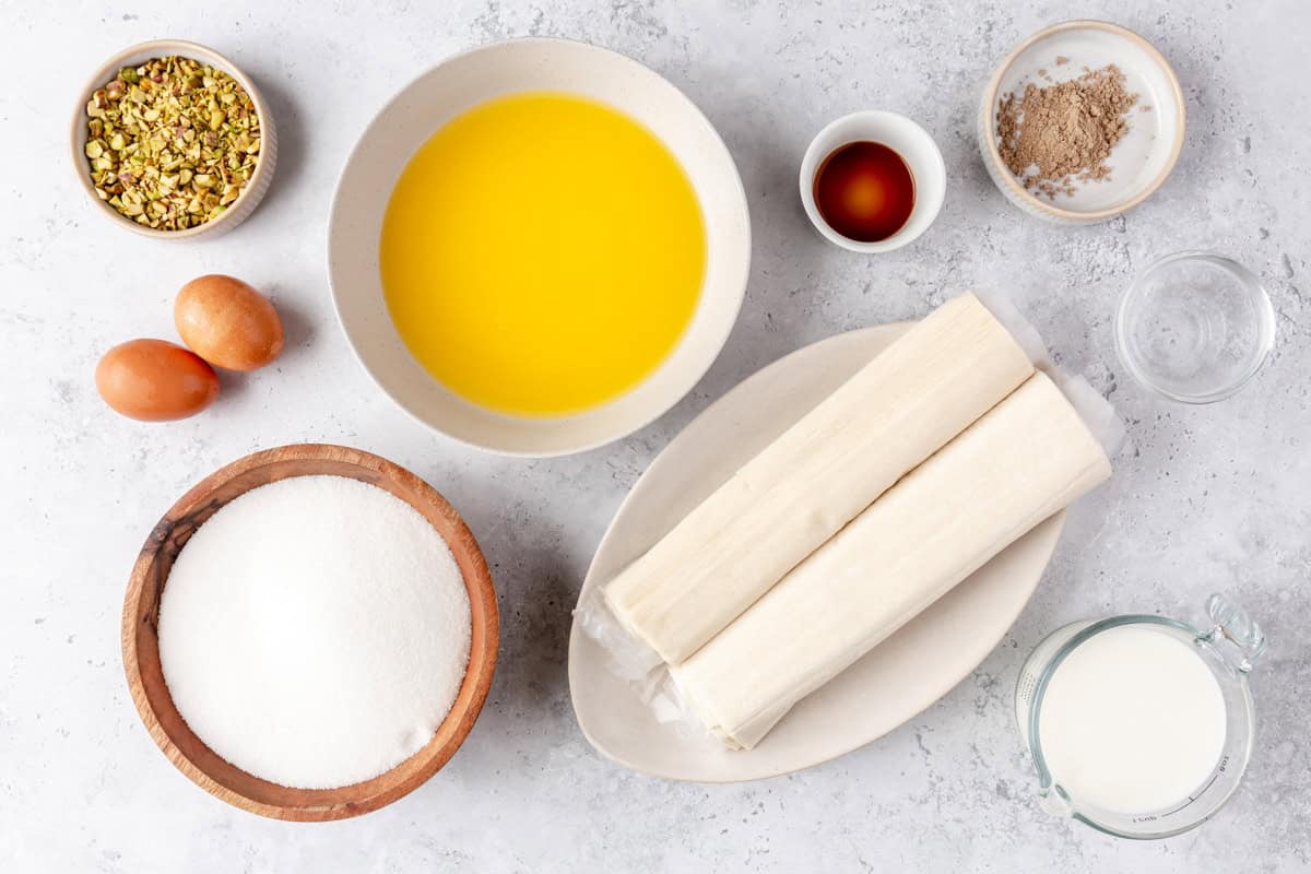 Ingredients for recipe before prepping: pistachios, eggs, melted butter, sugar, phyllo dough, vanilla, cardamom, rose water, and milk.