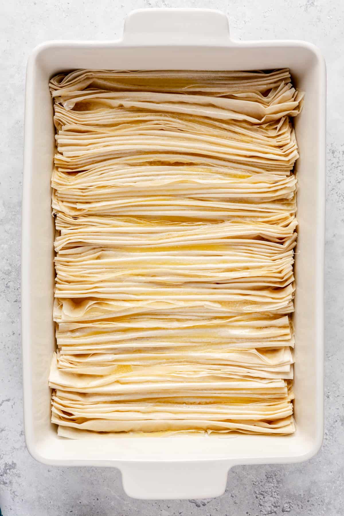 Layered phyllo dough in a baking dish brushed with melted butter.