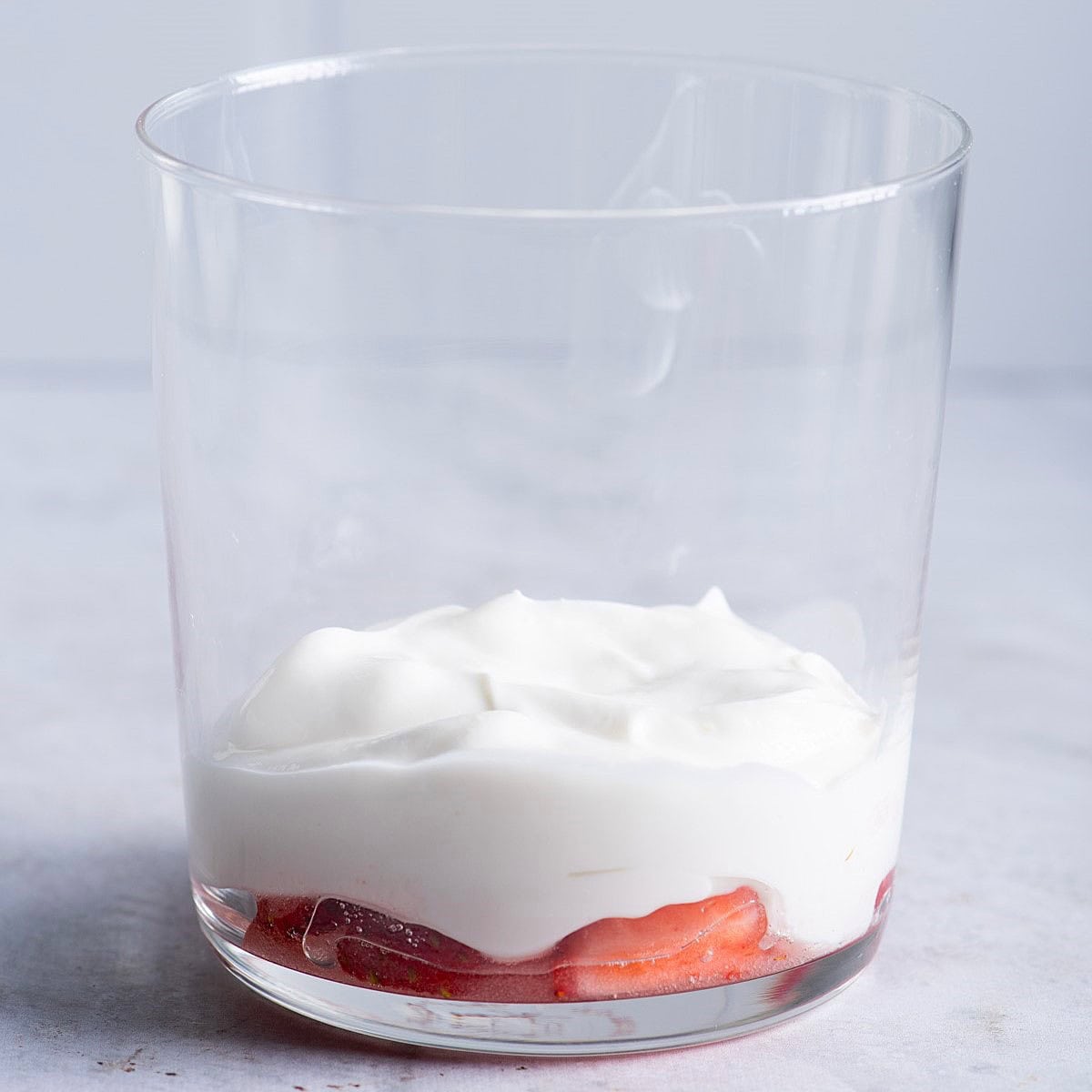 Adding the first layer of yogurt on top of fruit.