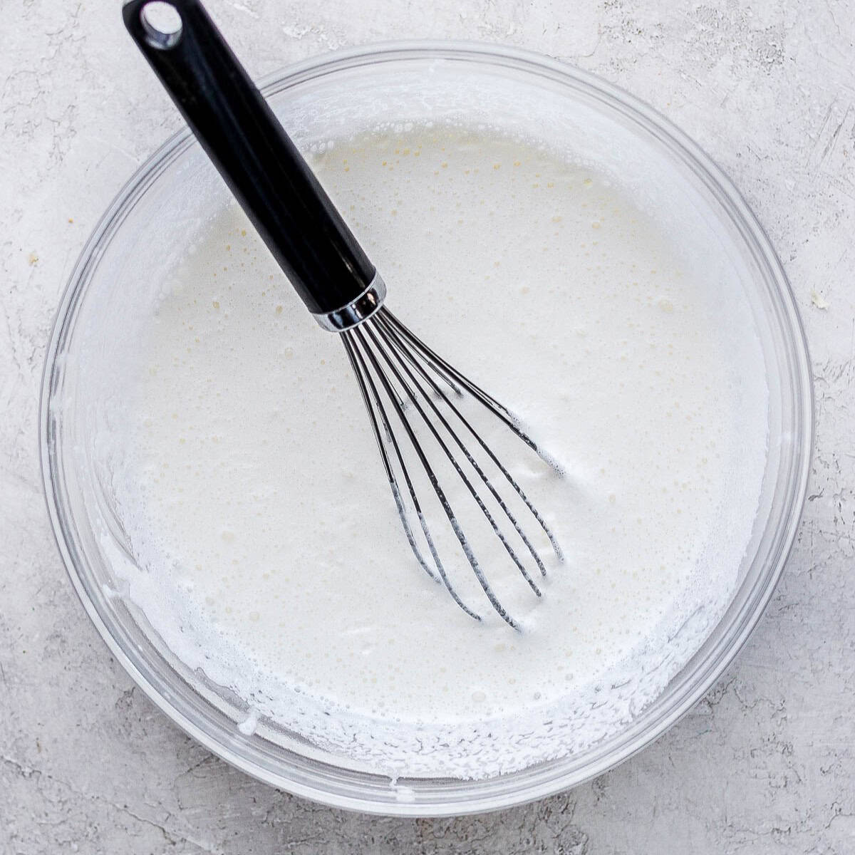 Heavy cream in a bowl with a whisk.