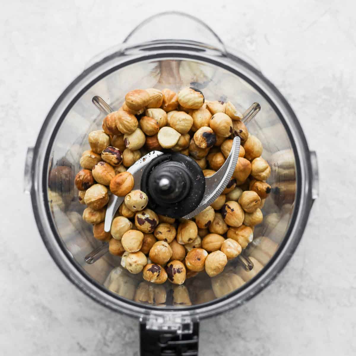 Roasted hazelnuts in the bowl of a food processor.