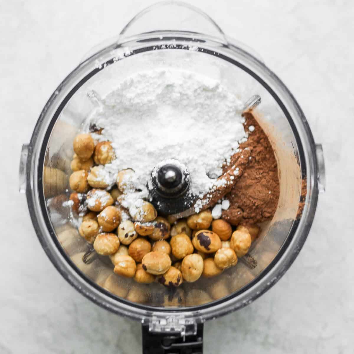 Cocoa powder, powdered sugar and salt added to food processor with hazlenuts.