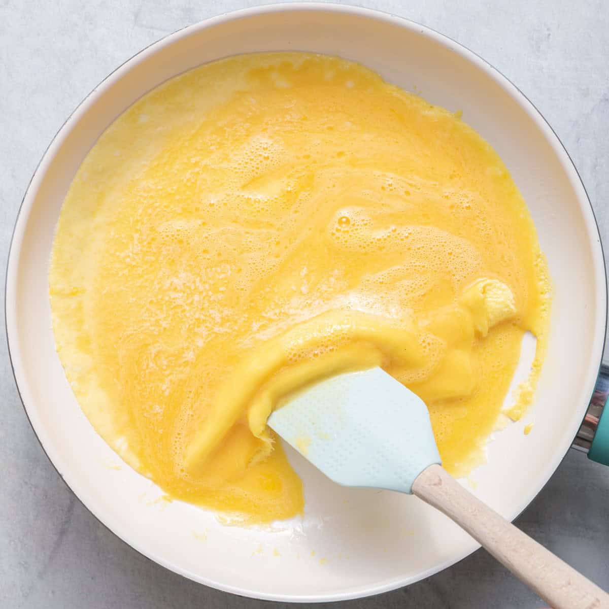 Rubber spatula pushing eggs in a pan.