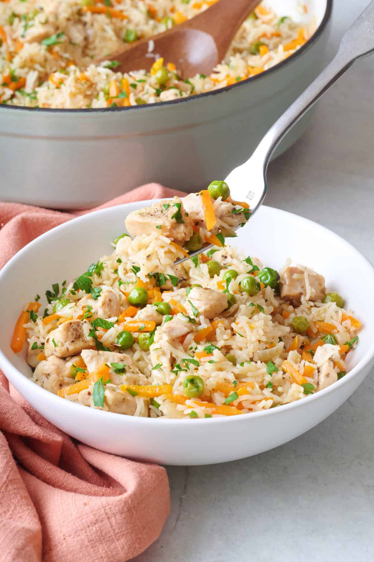 Fork lifting up a bite of chicken and rice with veggies with pot of more nearby.