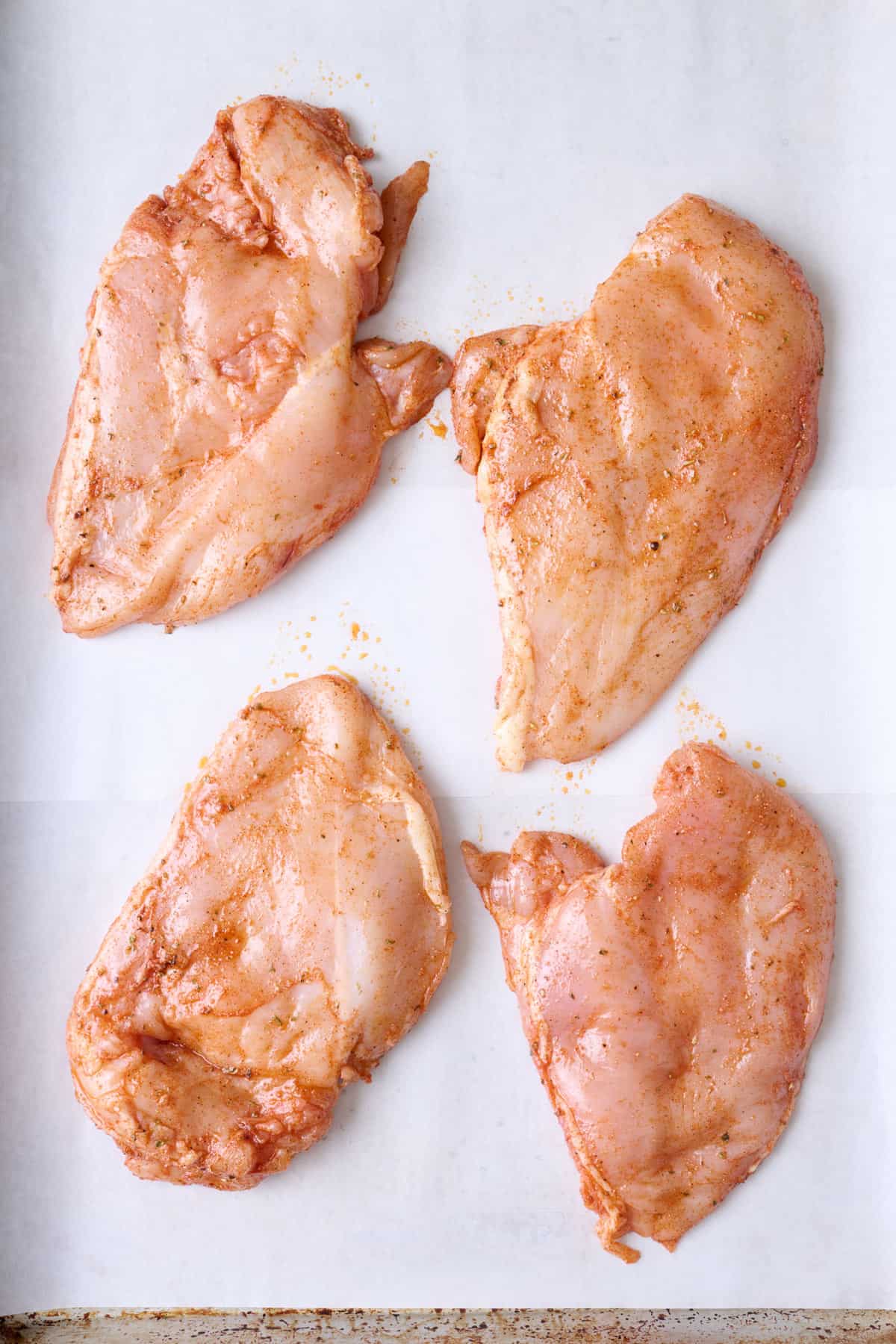 Seasoned chicken breasts on a parchment paper lined sheet pan before baking.