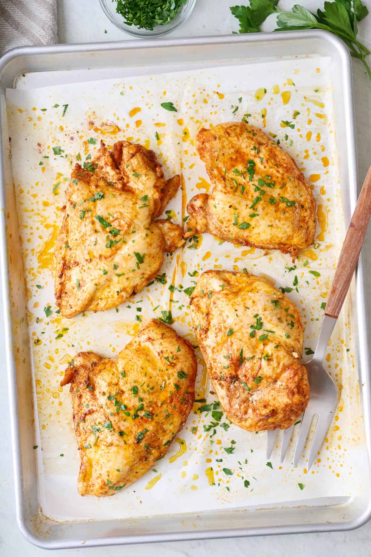 Oven baked chicken breasts on a sheet pan garnished with fresh parsley.