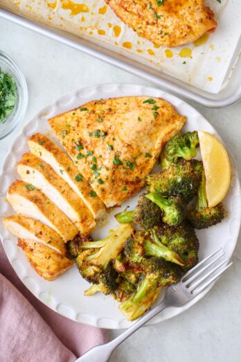 Oven baked chicken breast on a plate sliced half way with a side of roasted broccoli.