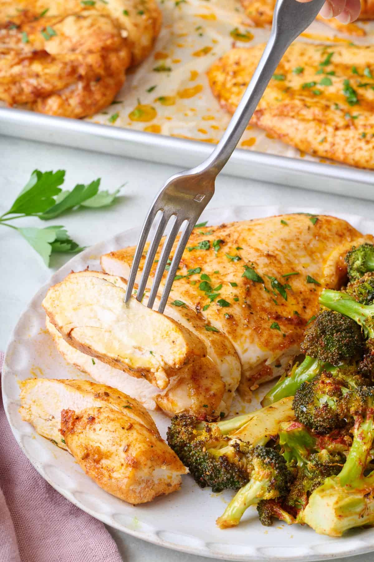 Fork lifting up a piece of baked chicken from a plate.