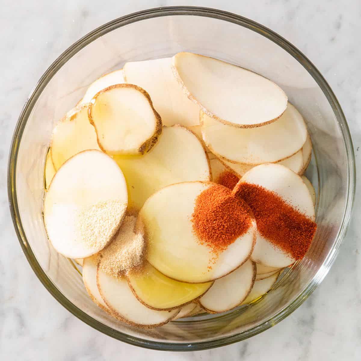 Sliced potatoes in a bowl with seasonings before tossing.