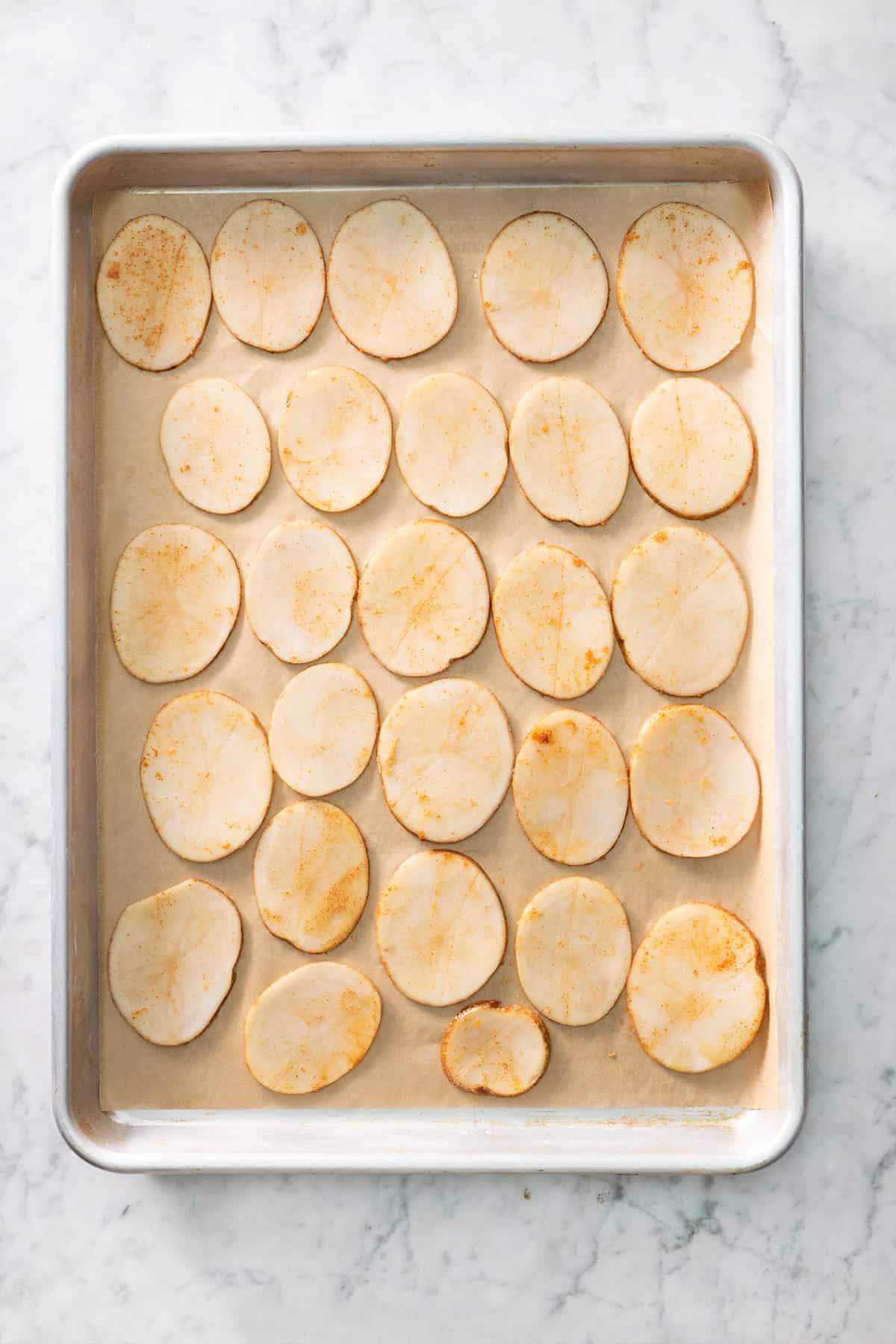 Seasoned potato slices on a parchment lined baking sheet before baking.