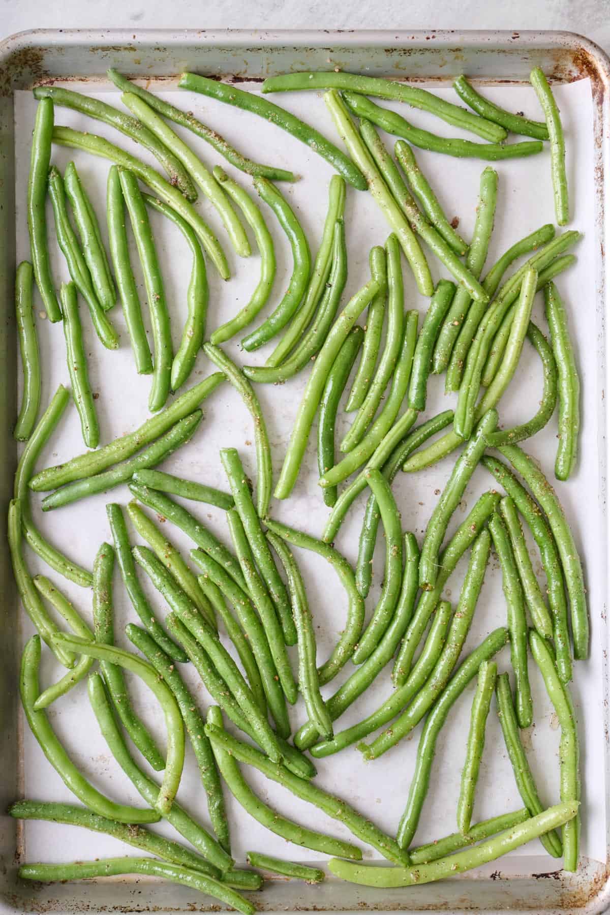 Seasoned green beans on a sheet pan before roasting.