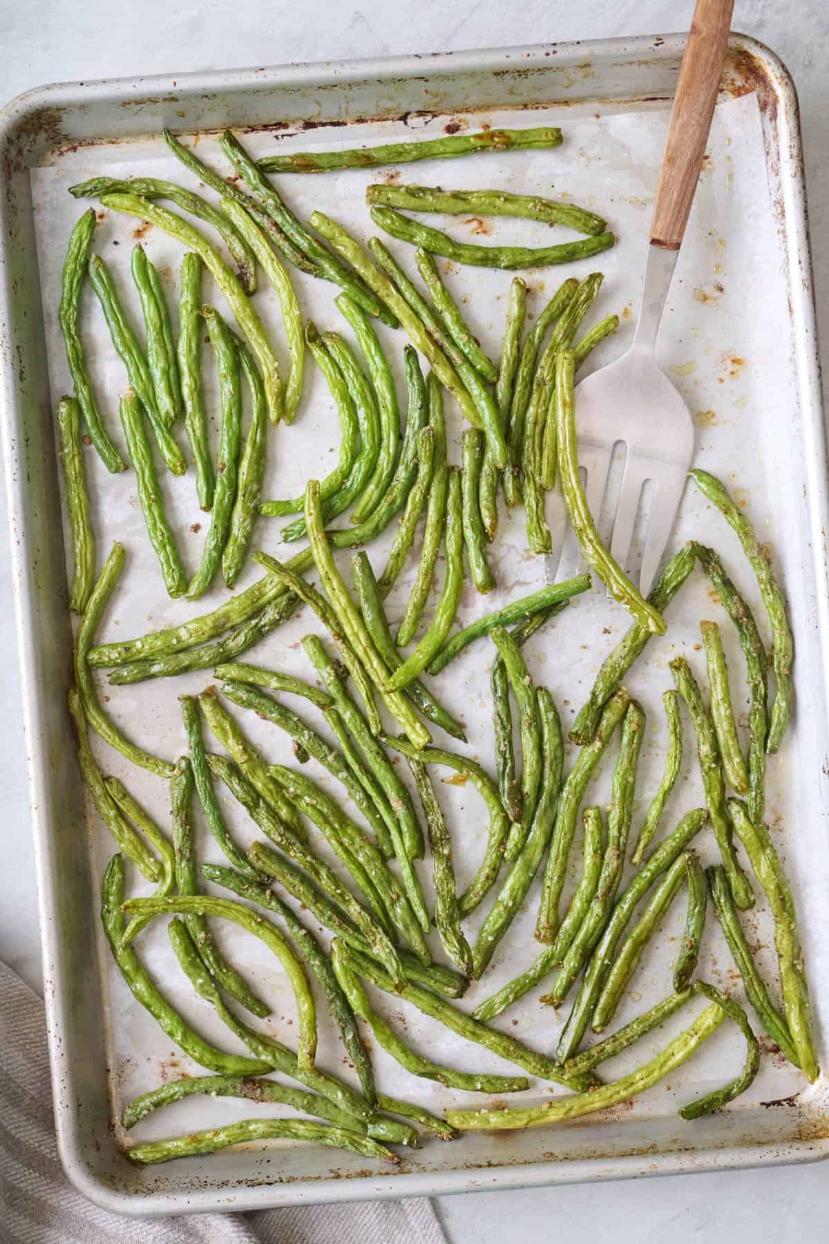 Roasted green beans on a sheet pan with a serving fork resting on pan.