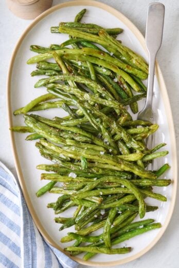 Roasted green beans garnished with flaky salt on a platter.