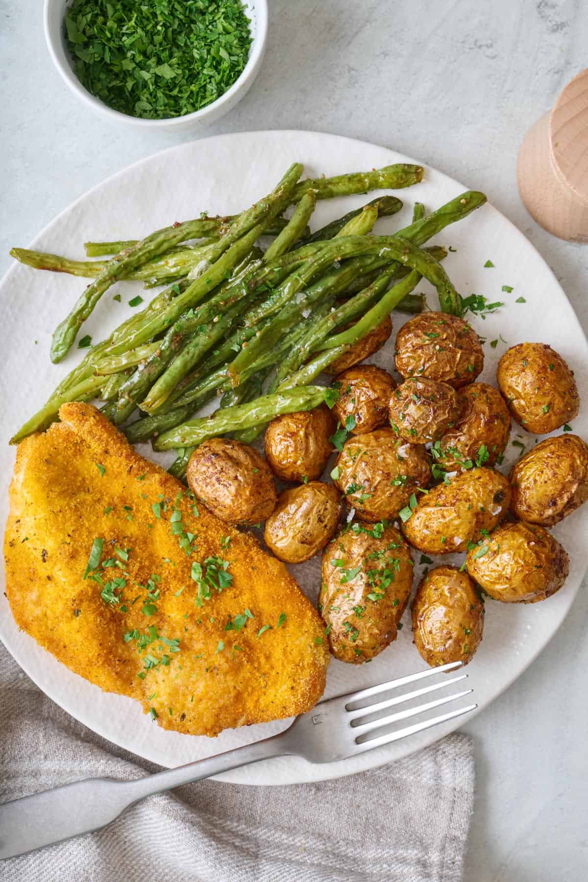 Serving of roasted green beans on a plate with breaded chicken and baby potatoes.