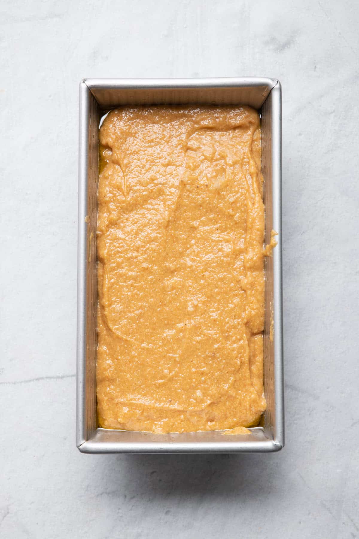 Bread batter added to a loaf pan before baking.