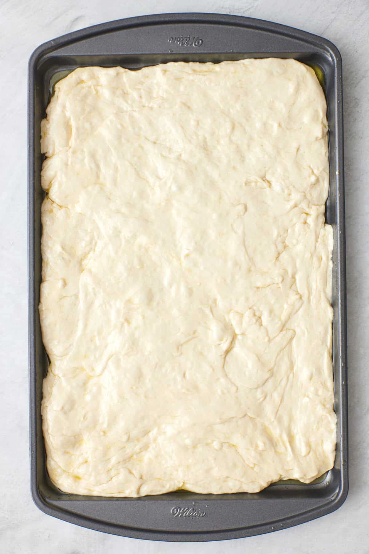 Dough after doubling in size on a greased sheet pan and pressed to the edges.