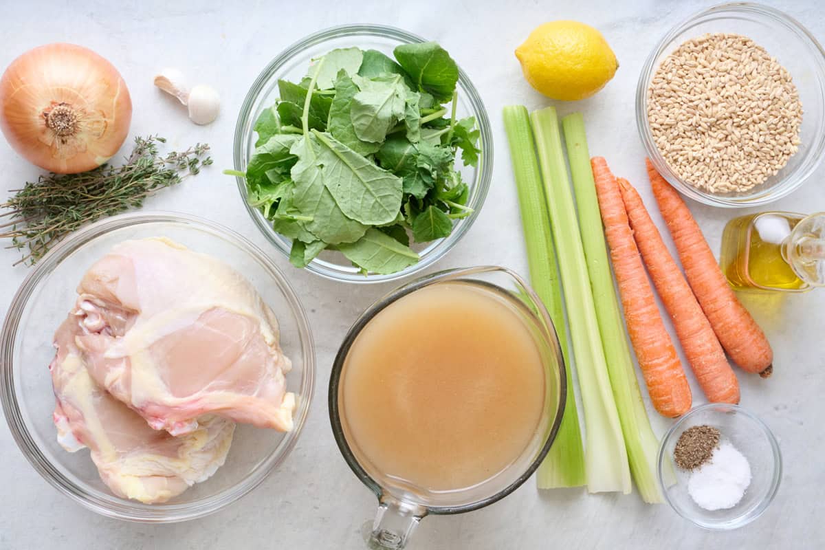 Ingredients for recipe before prepping: onion, thyme, chicken, kale, stock, celery, carrots, lemon, barley, oil, and seasonings.