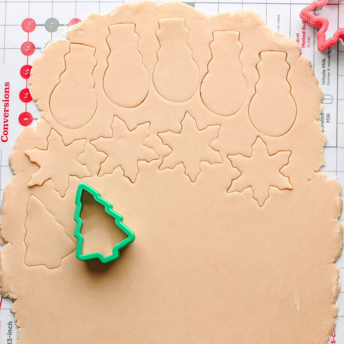 Cookie dough rolled out thin with Christmas themed cookies cut out with a cookie cutter.