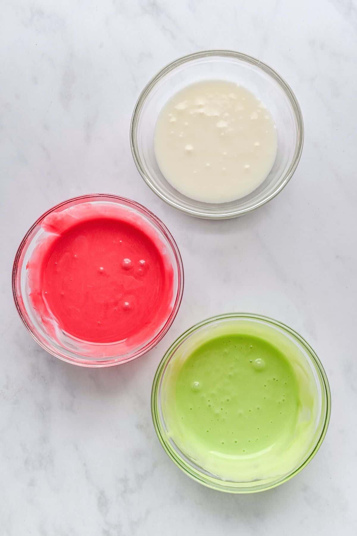 3 small bowls of icing with natural food dye added to two bowls, red and green.